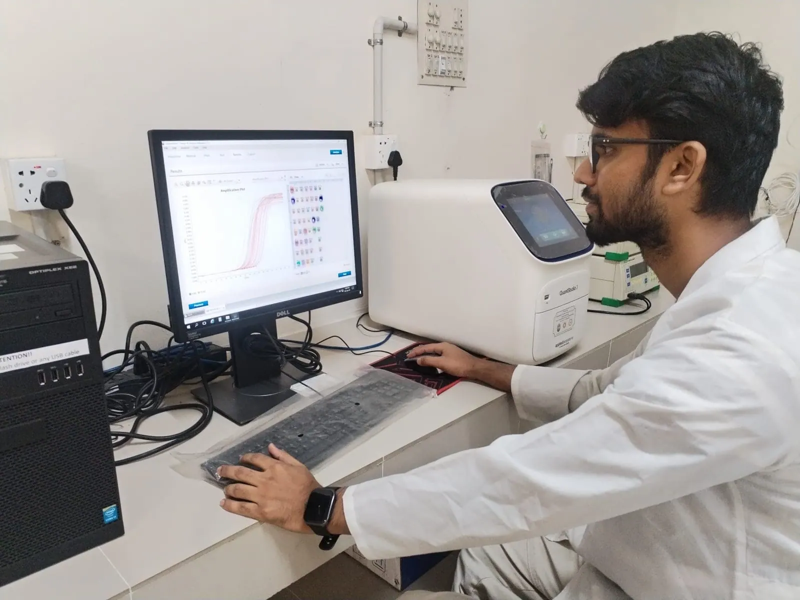 A BioPC researcher reading a real-time PCR amplification plot beside a QuantStudio thermal cycler